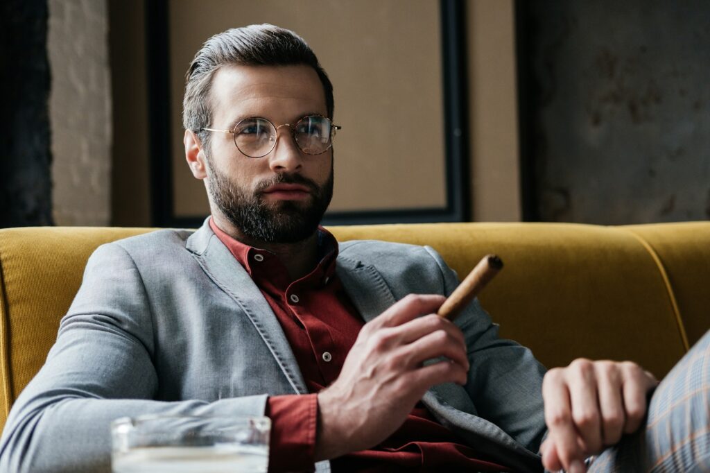 handsome bearded man with cigar and ashtray sitting on couch